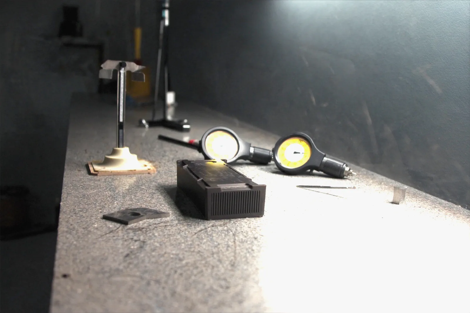 A moulded housing on the granite surface plate under a work light, with two dial indicators, a height gauge and gauge blocks set out around it.