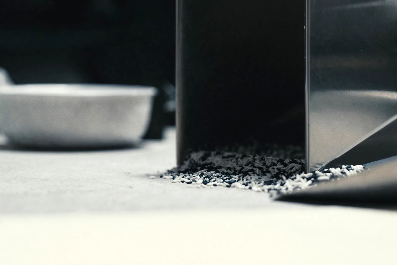 Black and white resin pellets spilled at the foot of a stainless hopper on the machine platen.