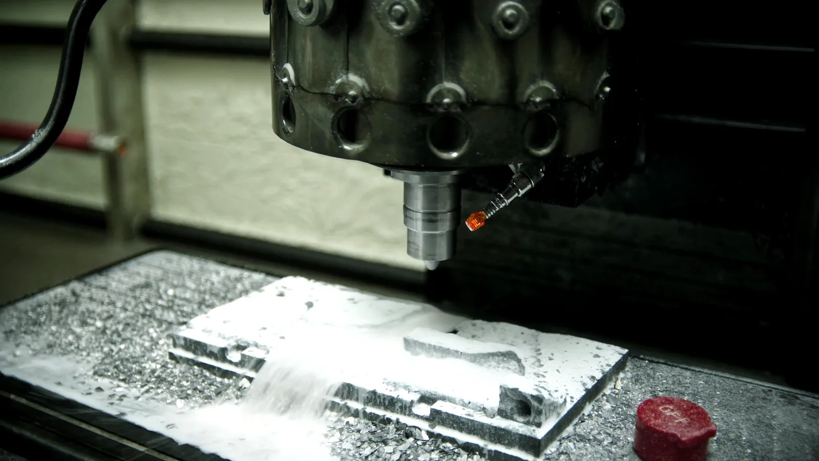 A carbide cutter roughing a cavity pocket into a P20 steel block on the CNC, coolant flooding the cut and chips banked around the plate.